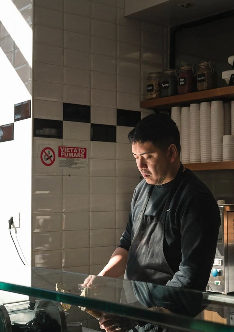 A barista preparing coffee in a traditional Roma cafe with bright natural lighting.